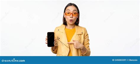portrait of stylish korean girl in sunglasses smiling pointing finger at smartphone screen