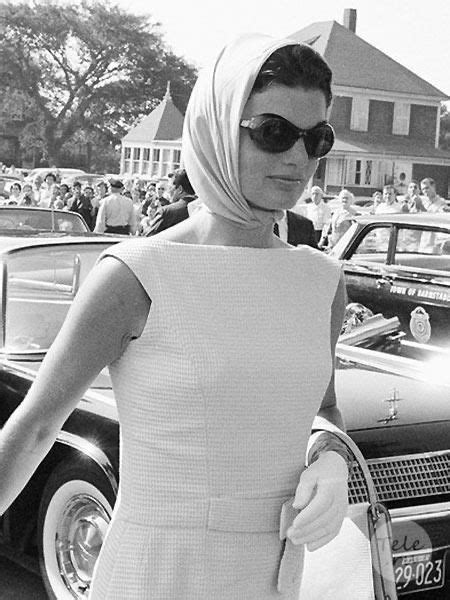 A Woman In A White Dress Is Standing Next To A Car And Holding A Purse