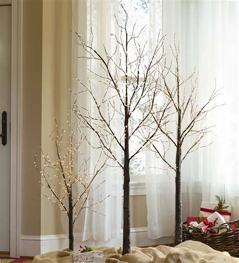 Two Small Trees In Front Of A Window With White Lights And Presents On