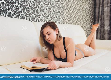 Woman Lying On A Sofa While Reading A Book In A Living Room Stock