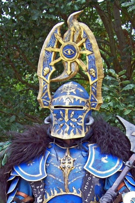 A Man Dressed In Blue And Gold Armor Holding Two Swords With Trees In