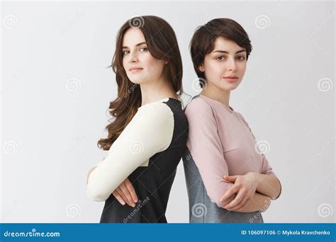 portrait of two lesbian girls with dark hair smiling standing backs to each other crossing