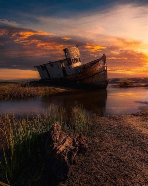 An Old Boat Sitting On The Shore At Sunset