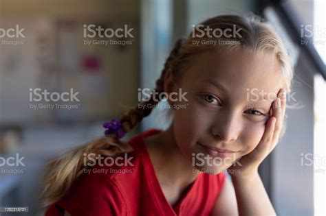 Schoolgirl With Blonde Hair In Plaits Looking To Camera In An Elementary School Classroom Stock