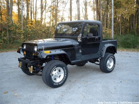 A Black Jeep Is Parked In A Parking Lot Next To Some Trees And Leaves