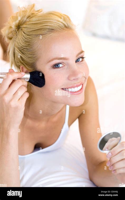 Female Blonde Hair Tied Up Wearing White Vest Top Lying Face Down On Bed Brushing Cheek Blusher