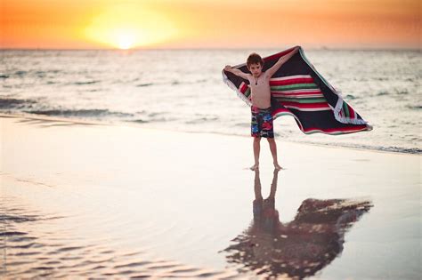 Boy Standing With An Outstretched Towel At The Beach At Sunset By Stocksy Contributor Angela