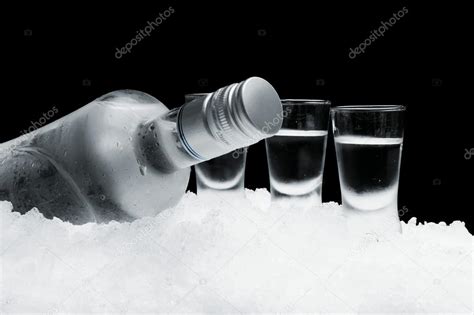 Bottle Of Vodka With Glasses Standing On Ice On Black Background Stock