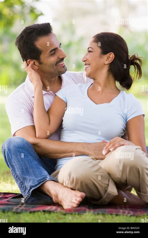 Couple Sitting Outdoors In Park Being Affectionate And Smiling