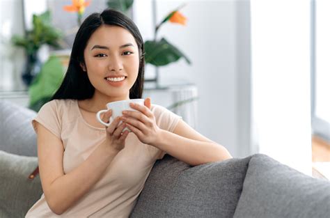 Portrait Of A Happy Beautiful Asian Brunette Girl Sitting On The Sofa