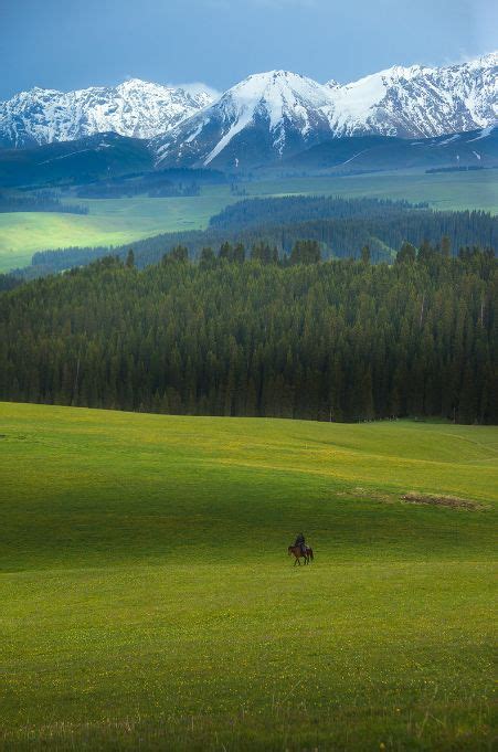 Two People Riding Horses In A Green Field With Mountains In The Backgrouds