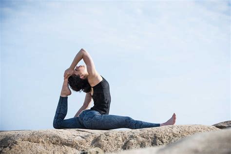 Woman One Legged King Pigeon Pose While Doing Yoga On Rock Against Sky