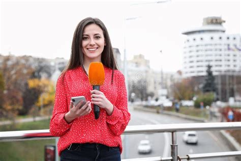 Young Female Journalist With Microphone And Smartphone Working On