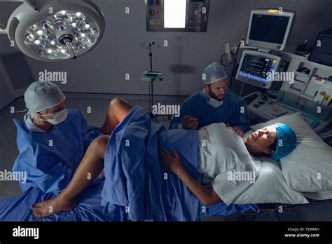 Surgeon Examining Pregnant Woman During Delivery While Man Holding Her Hand In Operating Room
