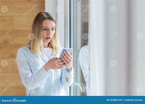 Young Woman Saw Bad News On Smartphone Standing By The Window In The