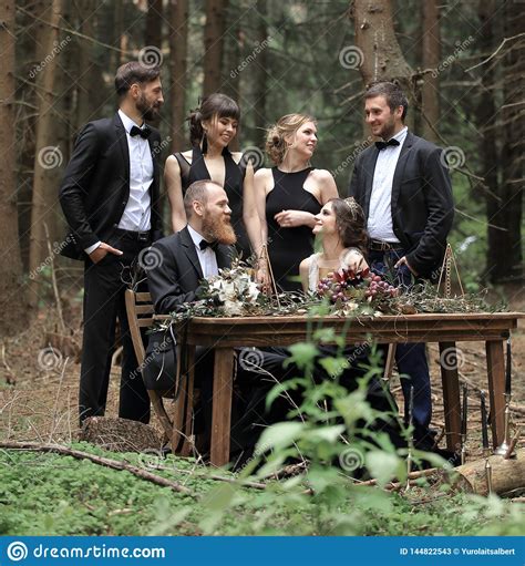 Guests And A Couple Of Newlyweds Near The Picnic Table In The Woods