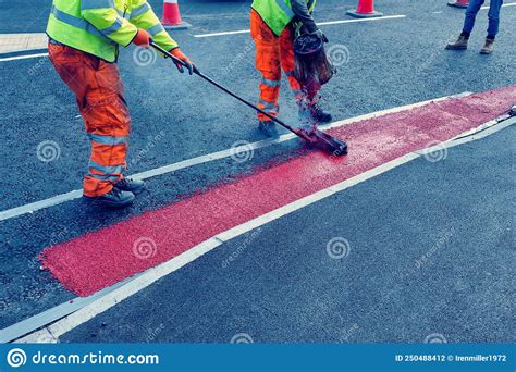 Road Workers Applying Hot Red Road Marking Paint On New Build Road