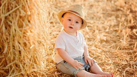 Very Cute Boy Child Baby Is Sitting On Paddy Straw Wearing White Blue