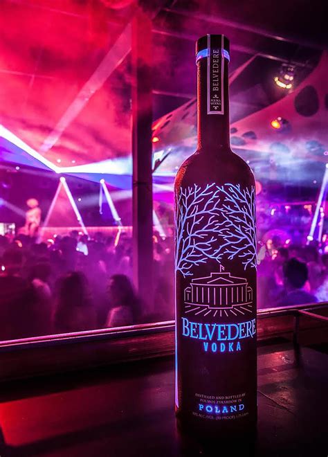 A Bottle Of Belveder Vodka Sitting On A Table In Front Of A Crowd