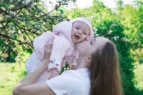 Young Mother Holds Little Laughing Daughter Over Nature Background