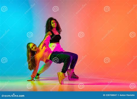 Two Stylish Modern Girls Dancing Hip Hop On Gradient Blue Orange Background In Neon Stock Image