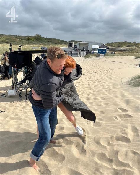 A Man Carrying A Woman On His Back In The Sand With Camera Equipment