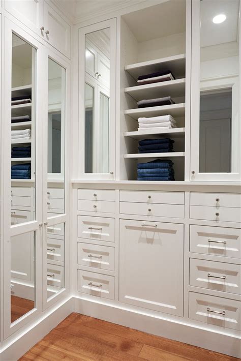 The Closet Is Full Of White Drawers And Large Mirrored Doors With Folded Blue Towels On Top
