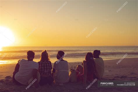 Vista Trasera De Diversos Amigos Sentados Juntos En La Playa Durante El