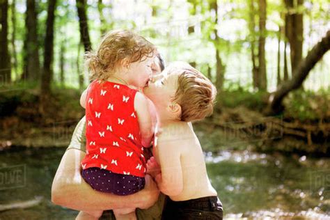Brother Kissing Sister Being Carried By Father At Forest Stock Photo