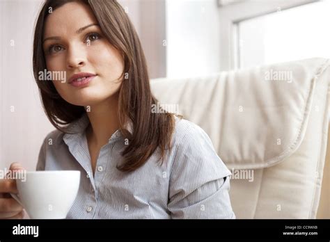 Young Woman At Home Sipping Tea From A Cup Sitting On Comfortable