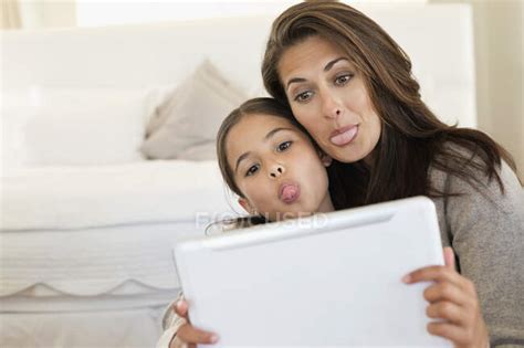 Woman And Her Daughter Making Their Faces In Front Of Digital Tablet