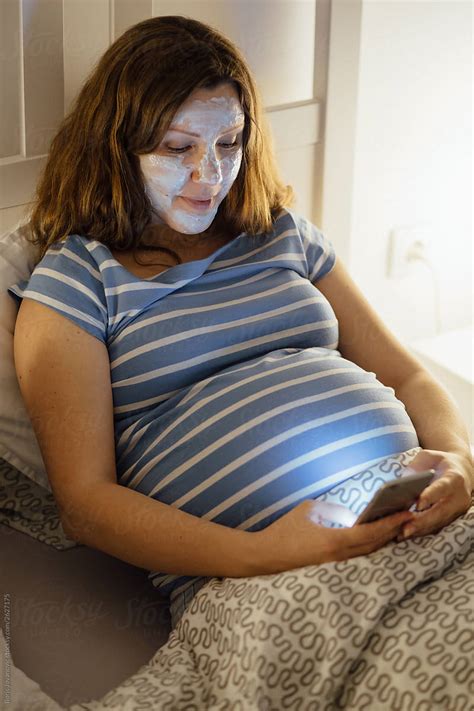Pregnant Woman Laying In Bed Using Her Phone By Stocksy Contributor