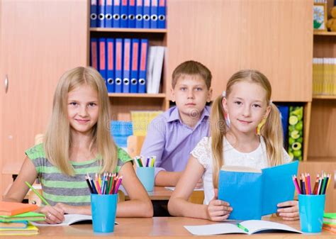 Happy Students Sitting At Their Desks In The Classroom Stock Photo