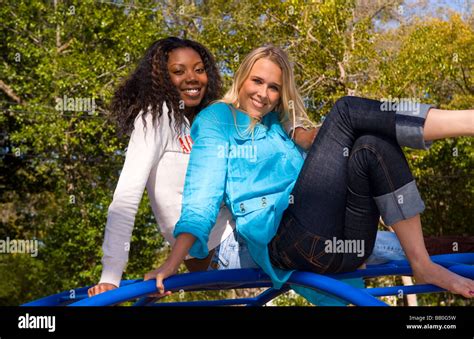 Black African American Woman And White Blonde Woman Friends On Bars Climbing In Outdoor Park