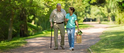 Caregiver Woman Helping Senior Man Outdoors In The Park Behavioral