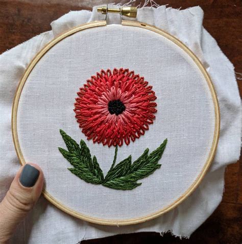 A Hand Embroidered Red Flower With Green Leaves