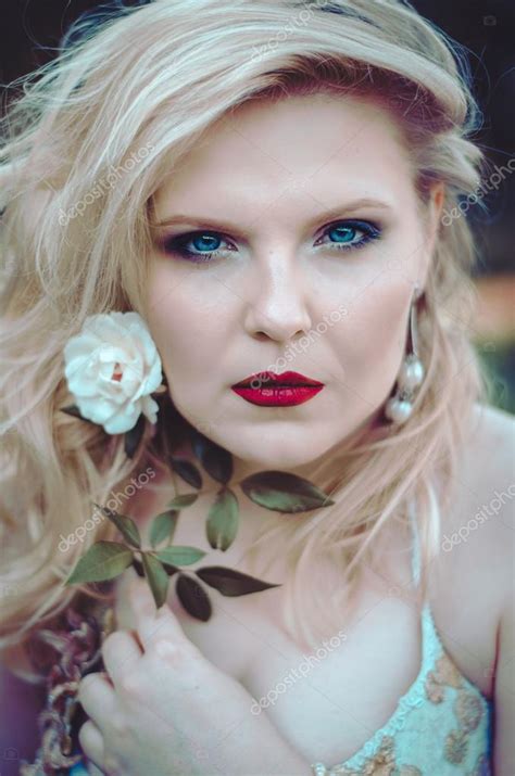 Portrait Of Blue Eyed Blonde Beauty With A Curvy Shape And Red Lips With A White Rose In His