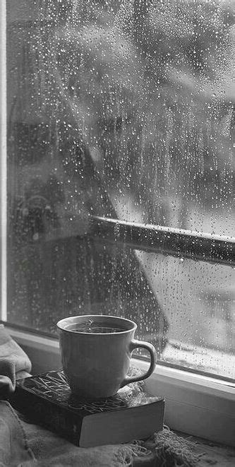 A Coffee Cup Sitting On Top Of A Book Next To A Window Covered In Rain