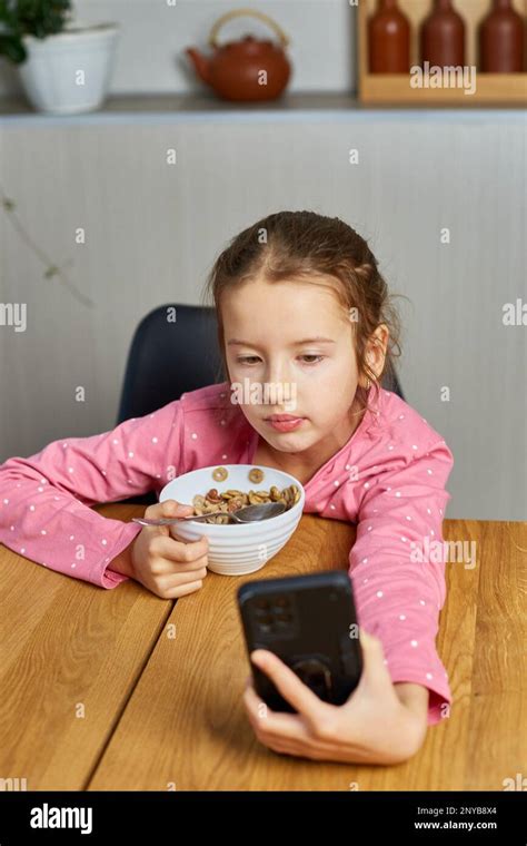 Little Girl Eating Cereal With Milk And Watching Video On Smartphone
