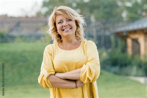 outdoor portrait of positive confident mature woman smiling female blonde in a yellow dress