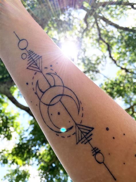 A Person S Arm With An Arrow And Compass Tattoo On It In Front Of Some Trees