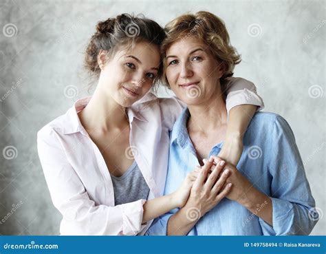 Beautiful Senior Mom And Her Adult Daughter Are Hugging Looking At Camera And Smiling At Home