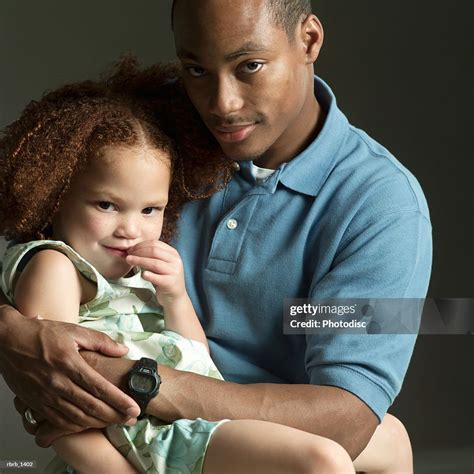 Studio Portrait Of An African American Father Smiling While Holding His