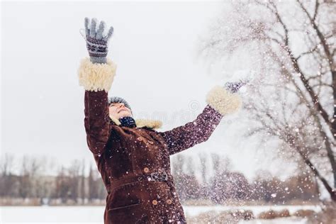 Happy Senior Woman Throwing Snow In Snowy Winter Park Having Fun