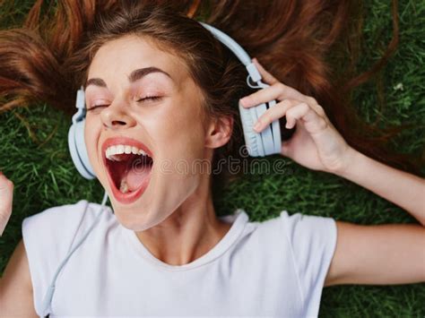 Woman Open Mouth Surprise Lying On Green Grass With Headphones Spread Her Hair On The Ground In