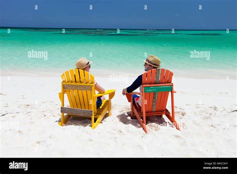 Happy Couple Sitting On Colorful Adirondack Chairs At Tropical Beach