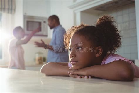 Sad Girl Listening To Her Parents Arguing In Kitchen Stock Photo