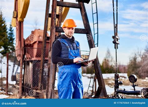 Oil Engineer With A Laptop Standing Next To An Oil Rig Making Notes In