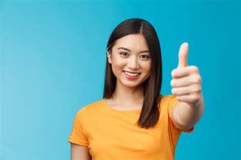 Premium Photo Cheerful Asian Female Model Showing Thumbs Up Gesture Smiling And Looking