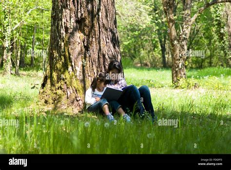 Girls Sitting Under Tree Reading A Book Stock Photo Alamy